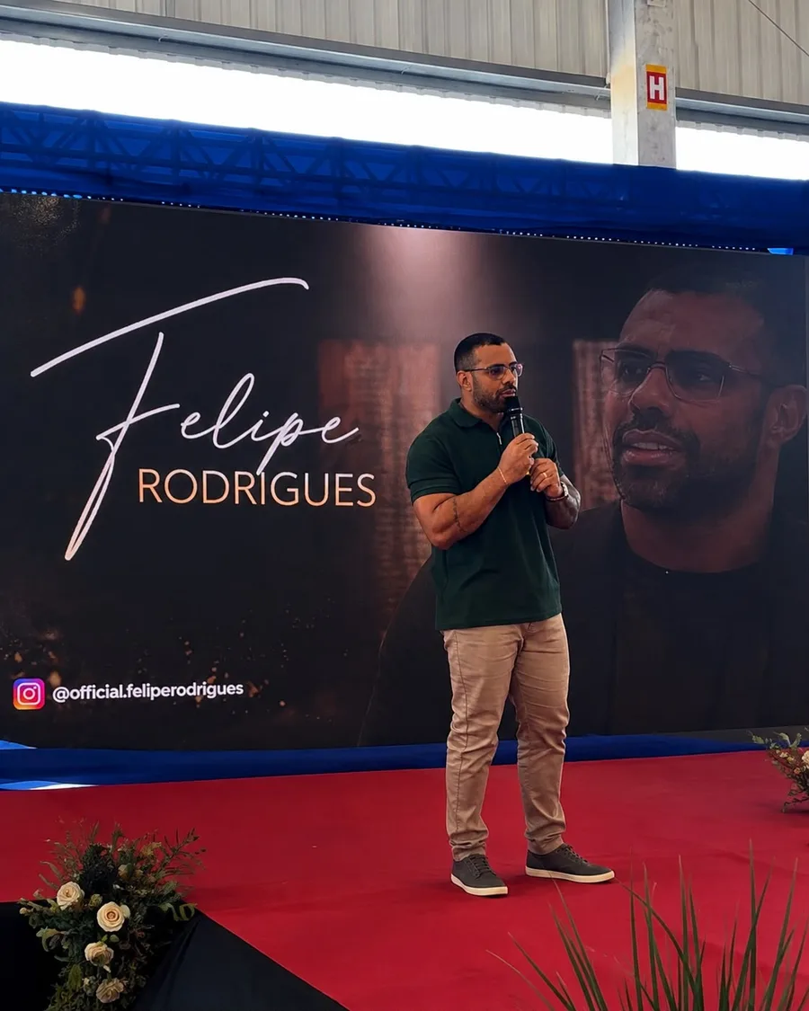 Felipe Rodrigues palestrando em evento, com seu nome no telão