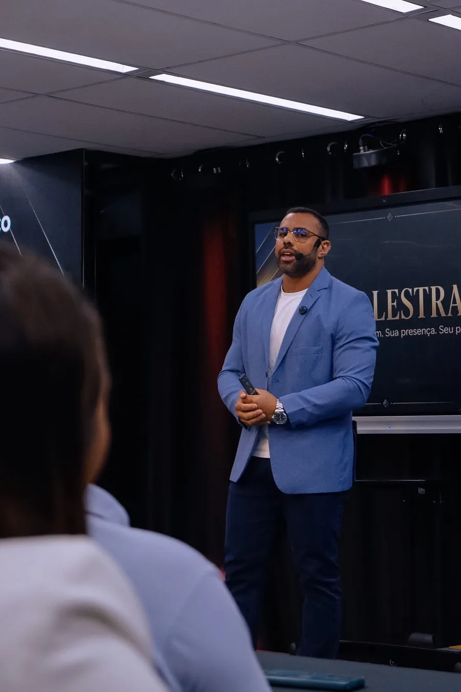 Felipe Rodrigues no palco, de blazer azul, apresentando a ideia de 1% de melhora por dia